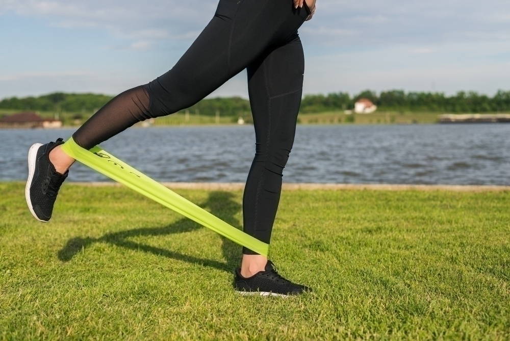 Athletic woman workout with resistance band outdoors. Fitness girl doing exercise for glutes at the park