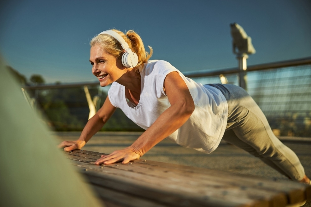 Beautiful sporty lady listening to music through wireless headphones and smiling while doing exercise on the street