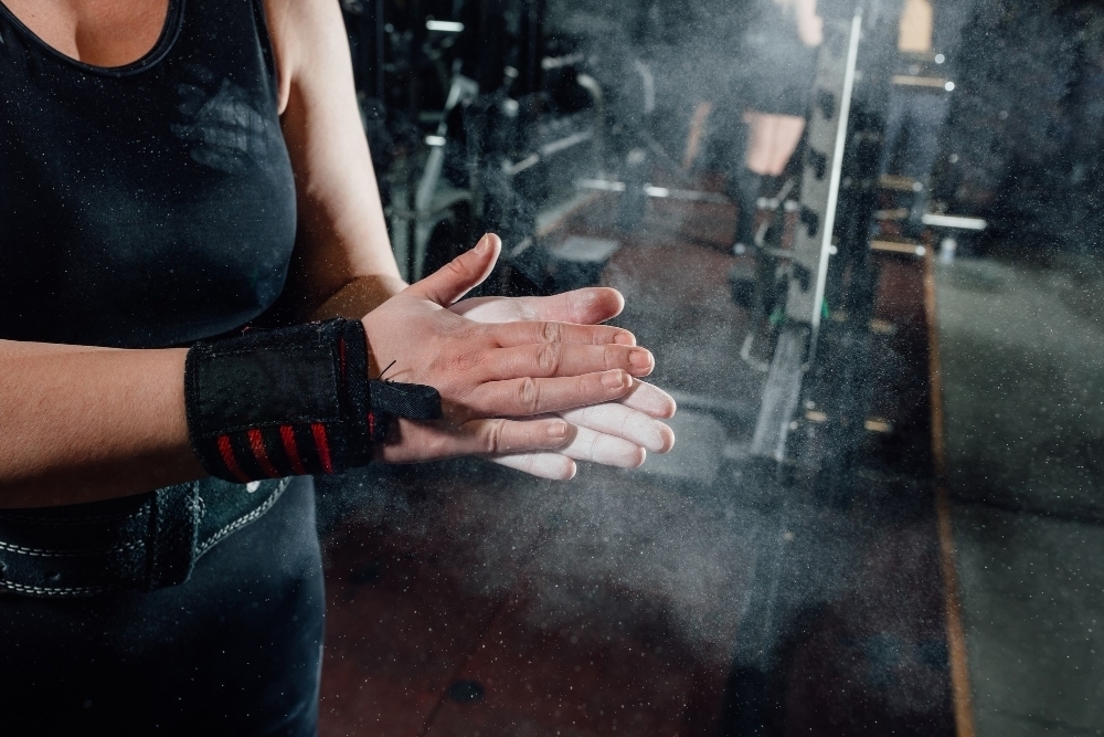 Cropped shot of young female athlete clapping hands with chalk powder before strength training