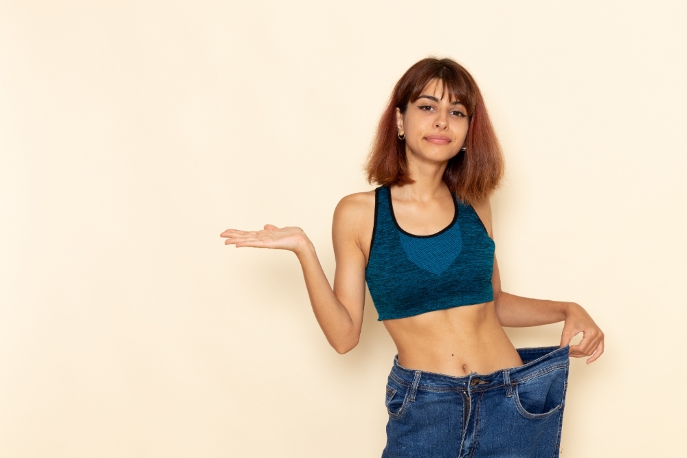 Front view of young female with fit body in blue shirt smiling on the light white wall