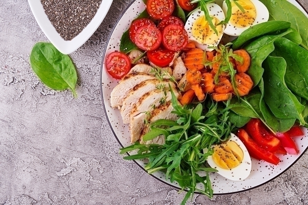 Plate with a keto diet food. Cherry tomatoes chicken breast eggs carrot salad with arugula and spinach. Keto lunch. Top view