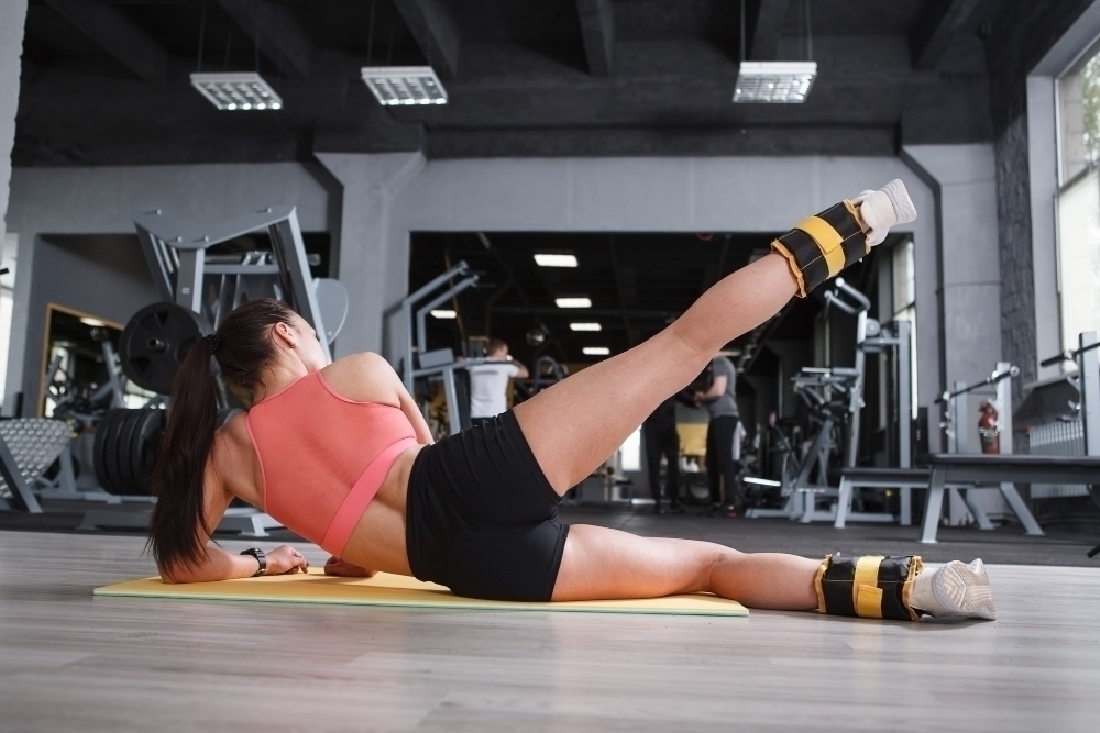 Rear view shot of a sportswoman with toned athletic body doing leg raise with ankle weights